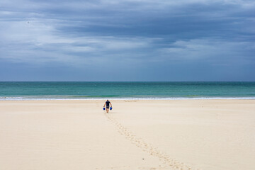 Fototapeta na wymiar A man carrying two buckets in the Victoria Beach in Cadiz, Spain.