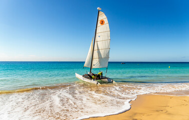 Two men are sailing in a sailboat from the beach to the sea 