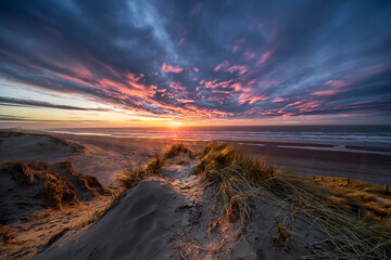 Stunning sunset on Dutch North sea coast with sand dunes and colouring clouds illuminated by golden...