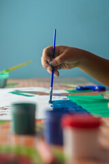 hand of a latin girl, painting a cardboard, with her brush
