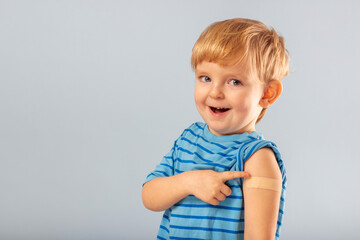 Vaccination of children. Happy vaccinated blonde kid boy showing arm with adhesive bandage after vaccine injection. Kids and covid-19 prevention, antiviral immunization - obrazy, fototapety, plakaty
