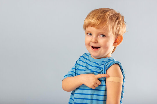 Vaccination of children. Happy vaccinated blonde kid boy showing arm with adhesive bandage after vaccine injection. Kids and covid-19 prevention, antiviral immunization