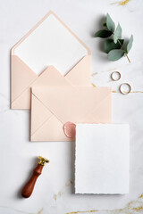 Wedding envelopes with invitation card mockup, wax seal stamp, golden rings on stone table. Wedding...