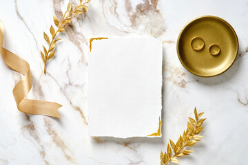 Wedding invitation card mockup, silk ribbon, golden rings and floral branches on marble table....
