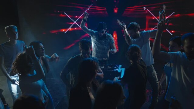 Cheerful people dancing around mixing console in club. Abstract video effects in background. Nightlife, modern music and entertainment concept.