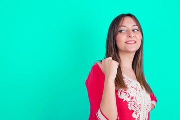 Charming young beautiful moroccan woman wearing traditional caftan dress over green background looking at copy space having advertisements