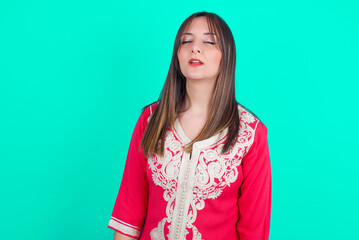 Fototapeta premium young beautiful moroccan woman wearing traditional caftan dress over green background looking sleepy and tired, exhausted for fatigue and hangover, lazy eyes in the morning.