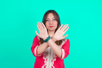 young beautiful moroccan woman wearing traditional caftan dress over green background has rejection expression crossing arms and palms doing negative sign, angry face.