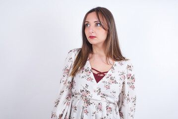 young Arab woman wearing floral dress over white background   stares aside with wondered expression has speechless expression. Embarrassed model looks in surprise