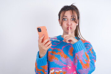  young arab woman wearing knitted sweater and ponytail over white background holding modern gadget ask not tell secrets