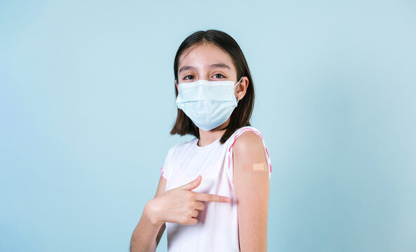 Latin Girl Child Wearing Face Mask After Getting A Vaccine Protection The Coronavirus And Showing Arm With Bandage After Receiving Vaccination On Blue Background