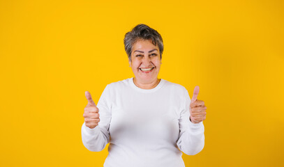 latin matured woman portrait with thumbs up on yellow background in Mexico Latin America - obrazy, fototapety, plakaty