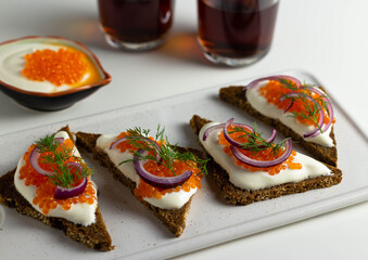 Sandwiches with red caviar on pieces of rye bread on a white ceramic board.
