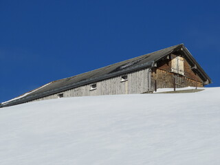 Idyllic Swiss alpine mountain huts dressed in winter clothes and in a fresh snow cover on slopes on the Alpstein mountain range - Mountain pass Schwägalp, Switzerland (Schweiz)