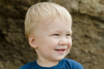 A smiling little boy - toddler is a blonde close-up portrait outdoors. 