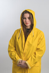 Portrait of a girl dressed in raincoat posing with hood on her head and looking at camera isolated over white background. Caucasian. Brunette. Piercing.