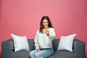 Serious woman show stop gesture, protest against gender discrimination, sitting on sofa. Woman...