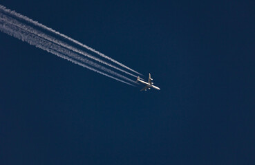 Airplane with four stream condensation trail against blue sky
