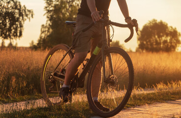 Cyclist on a gravel bike riding a trail in a field at sunset.