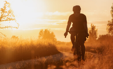 Silhouette of a cyclist on a gravel bike riding a countryside trail at sunset.