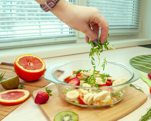 A woman's hand sprinkles a fruit salad with herbs. Salad dressing. Healthy eating at home.
