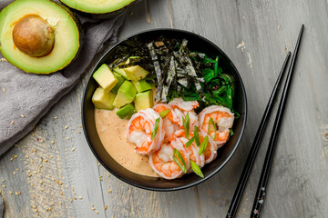 Poke with shrimps, avocado, chukka and sauce with rice on black bowl on grey wooden table top view