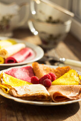 Multicolored flat pancakes on a plate decorated with raspberries. Original food pancakes on Maslyanitsa