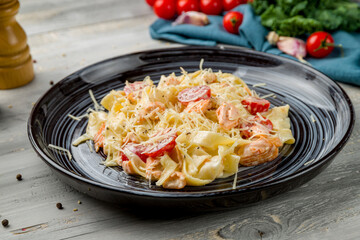 tagliatelli pasta with salmon and tomatoes with creamy sauce and parmesan on grey wooden table
