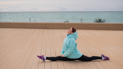 Caucasian woman in a sweatshirt stretches on the split outdoors. 