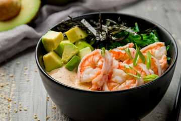 Poke with shrimps, avocado, chukka and sauce with rice on black bowl on grey wooden table macro close up