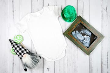 Baby romper onesie and sonogram product mockup. St Patrick's Day farmhouse theme SVG craft product mockup styled with green leprechaun hat and buffalo plaid gnome against a white wood background.