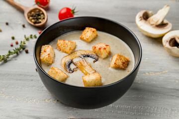 Cream soup of mushrooms with croutons on black bowl on grey wooden table