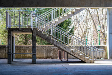 Concrete and metal stairs in covered parking lot with winter branches and green streetlamps in distance