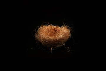 Small bird's nest made of dry grass on a black isolated background, side view 
