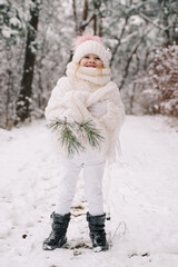 Beautiful little girl in a white sweater in a white hat. Little girl in a snowy forest. Christmas time.