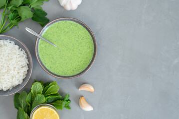 Healthy fresh green chutney sauce. With fresh mint pudina and yogurt. Spicy indian cuisine. Served with rice, lemon, garlic and parsley. Top view, grey background, copy space - obrazy, fototapety, plakaty
