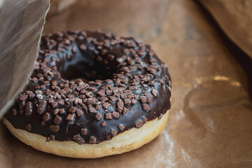 Selective focus on chocolate toppings on the donut. Fresh chocolate doughnut on the wooden table. Close up of chocolate donut on the table