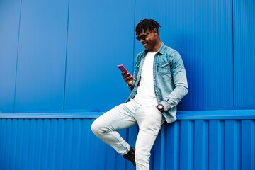african american man in stylish clothes and sunglasses browsing social media photos on mobile phone...