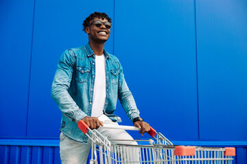 Arican American man , running with shopping cart. man is shopping in the city and smiling while walking near the mall