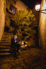 zufriedener lachender Geschäftsmann sitzt am Laptop und gibt Handzeichen, Stein-Treppe in Altstadt-Gasse, Nacht, Hochformat