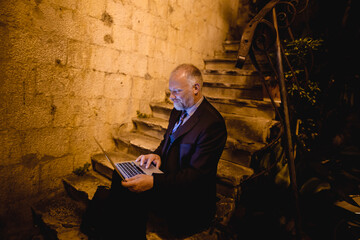lächelnder Geschäftsmann sitzt mit Laptop auf einer alten Stein-Treppe, Nacht