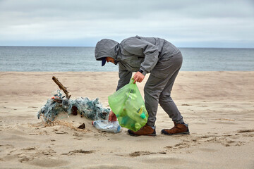 male volunteer collects debris thrown by a storm on a sandy beach