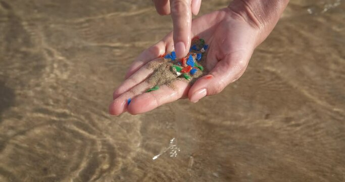 Plastic pollution in wildlife. A girl show her hands with sand and microplastic from water. A concept of microplastic pollution in world ocean.