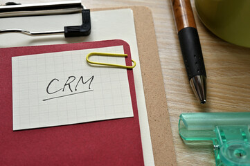 A piece of paper clipped to the edge of the red notebook has CRM written on it. It is an...