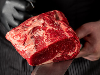 Close up beef meat in chef butcher's hands with knife on black background - 486161729