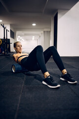 Fototapeta na wymiar Motivated physically disabled sportswoman uses foam roller while exercising at gym.