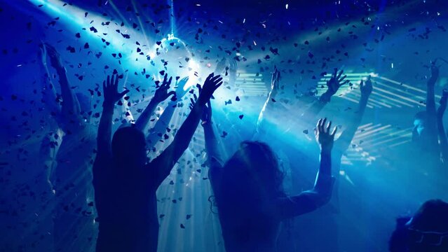 Young people enjoying time at disco. Dancing in falling confetti. Nightlife, modern music and entertainment concept.