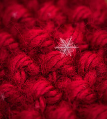 Macro close up of single snowflake against red wool background.