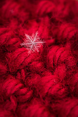 Macro close up of single snowflake against red wool background.