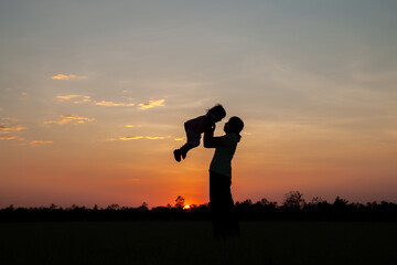 silhouette of mother raising her child at sunset
